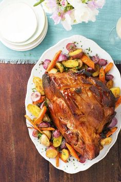 a large piece of meat is on a plate with potatoes and carrots next to a glass of wine