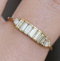 a close up of a person's hand wearing a gold ring with baguettes