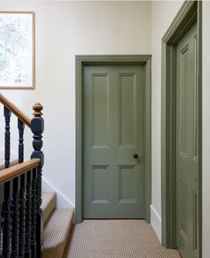 a green door in a white room next to a banister and stair case with black handrails