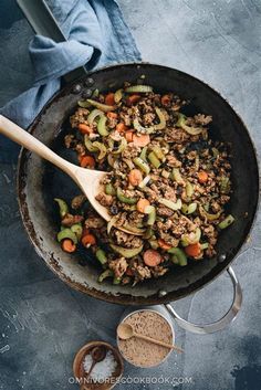 a skillet filled with ground beef, carrots and celery next to a wooden spoon