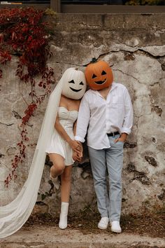 a man and woman dressed up as pumpkins standing next to each other in front of a stone wall