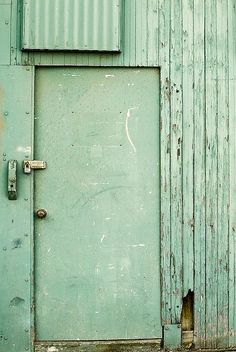 an old green door is open in front of a blue building with peeling paint on it