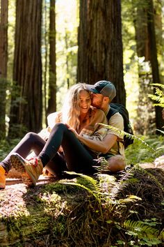 a man and woman sitting on the ground in the middle of a forest hugging each other