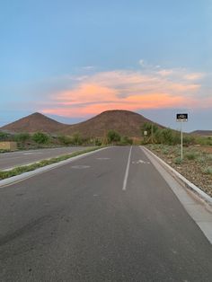 an empty road with mountains in the background at sunset or sunrise, as seen from across the street