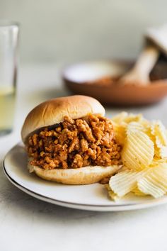 a sloppy joe sandwich on a plate next to potato chips and a glass of water