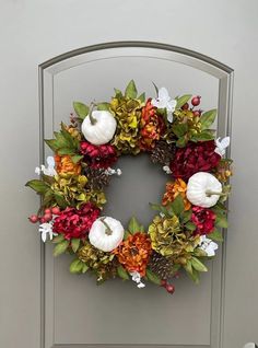 a wreath with white pumpkins, flowers and leaves on it is hanging on the front door