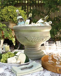 an outdoor table with wine glasses, cheese and other food items on top of it