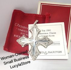 a small silver cross on a red cloth with a white card in the background and an old - fashioned christmas ornament