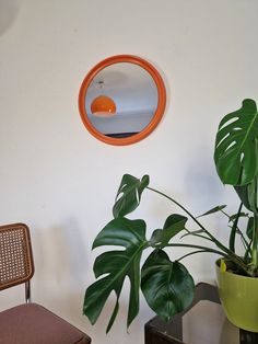 an orange circle mirror hangs on the wall above a chair and table with a potted plant