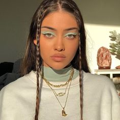 a woman with braids on her head wearing a white sweater and gold necklace, looking at the camera