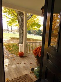 an open door leading to a porch with fall leaves on the ground and trees in the background