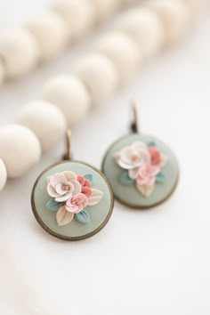 two earrings with flowers on them sitting next to white bead necklaces and beads