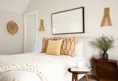 a white bed with pillows and blankets on top of it next to a wooden table