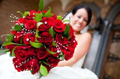 a bride holding a bouquet of red roses in front of her face and smiling at the camera