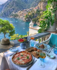 a table with pizza and drinks on it overlooking the water's edge in italy