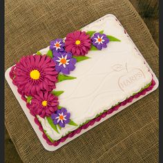 a cake with flowers on it sitting on a chair in front of a tablecloth