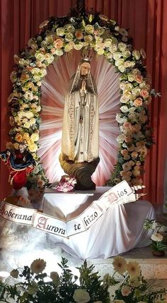 a statue of the virgin mary is surrounded by flowers and wreaths in front of a red curtain