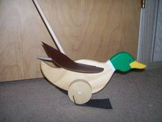 a wooden toy duck with a green beak and brown wing sitting on the floor next to a door