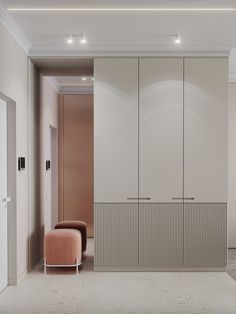 an empty room with white cabinets and a pink chair in the middle, next to a beige couch