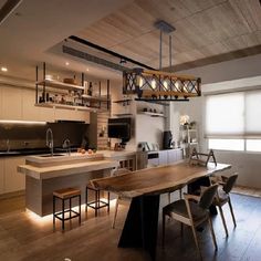 an open kitchen and dining area with wooden floors, white walls and ceiling lights above the island