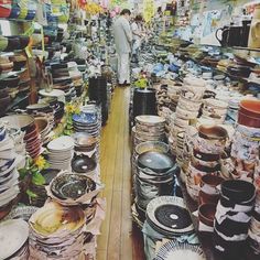 there are many stacks of plates on the floor in this store, and one person is standing behind them