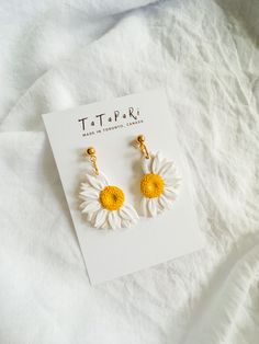 a pair of yellow and white daisy earrings sitting on top of a card with the tag tark