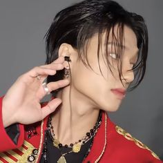 a man with black hair wearing a red jacket and gold jewelry on his neck is holding a cell phone to his ear