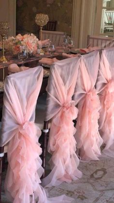 a dining room table with chairs covered in pink chiffon sashes and place settings