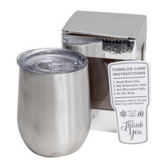 a stainless steel tumbler with a thank you label on the side and a silver box behind it