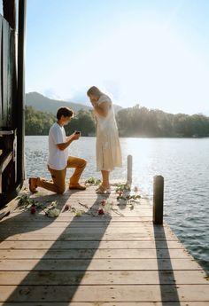 a man kneeling down next to a woman on a dock near the water with flowers