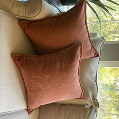 two pillows sitting on top of a white couch next to a potted palm tree