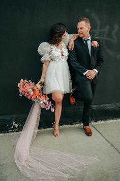 a man and woman standing next to each other in front of a wall with flowers