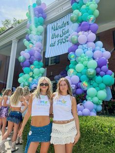 two women standing in front of a balloon arch