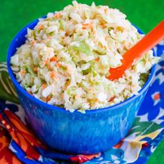 a blue bowl filled with coleslaw on top of a colorful cloth next to an orange spoon