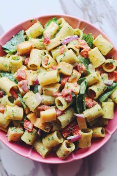 a pink bowl filled with pasta and vegetables