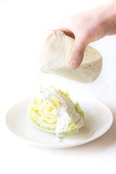 someone pouring dressing onto a salad on a white plate