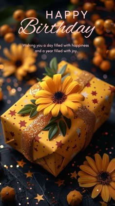 a birthday card with a yellow gift box and sunflowers on the table next to it