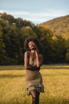 a woman is standing in the grass talking on her cell phone while wearing a polka dot dress