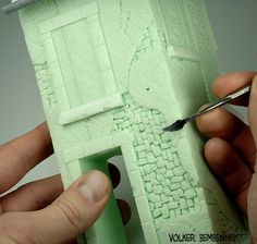 someone is painting the outside of a small house with green paint and a pair of scissors