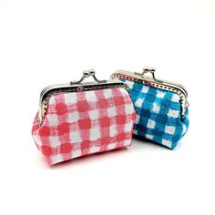 two small purses sitting next to each other on a white surface, one is pink and the other is blue