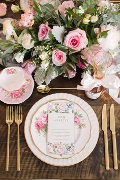 a table setting with pink flowers and gold place settings