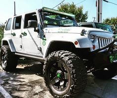 a white jeep is parked on the side of the road with green lettering and tires