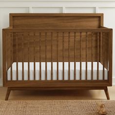 a wooden crib with white sheets in a room next to a rug and wall