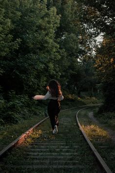 a woman is running down the railroad tracks with her arms outstretched in front of her