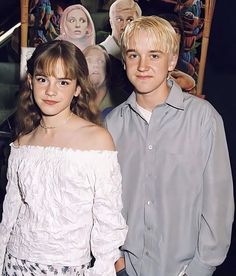 two young people standing next to each other in front of a movie poster on the wall