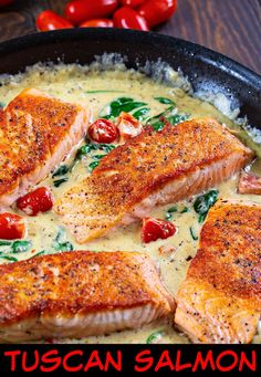 some salmon fillets are in a skillet with tomatoes and spinach on the side