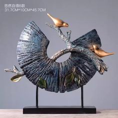 a metal sculpture with two birds on it's back and one bird sitting on top of the other