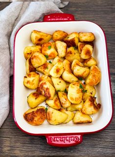 a red and white casserole dish filled with potatoes on top of a wooden table