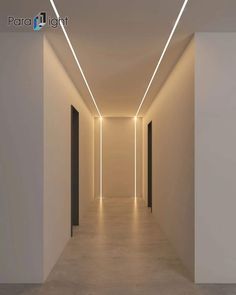 an empty hallway with white walls and lights on the ceiling is lit by recessed lighting