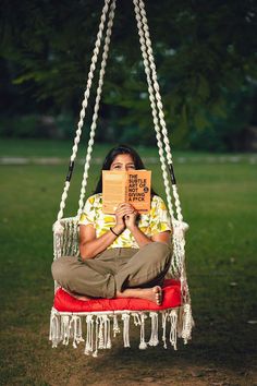 a woman reading a book while sitting in a hammock with chains hanging from it